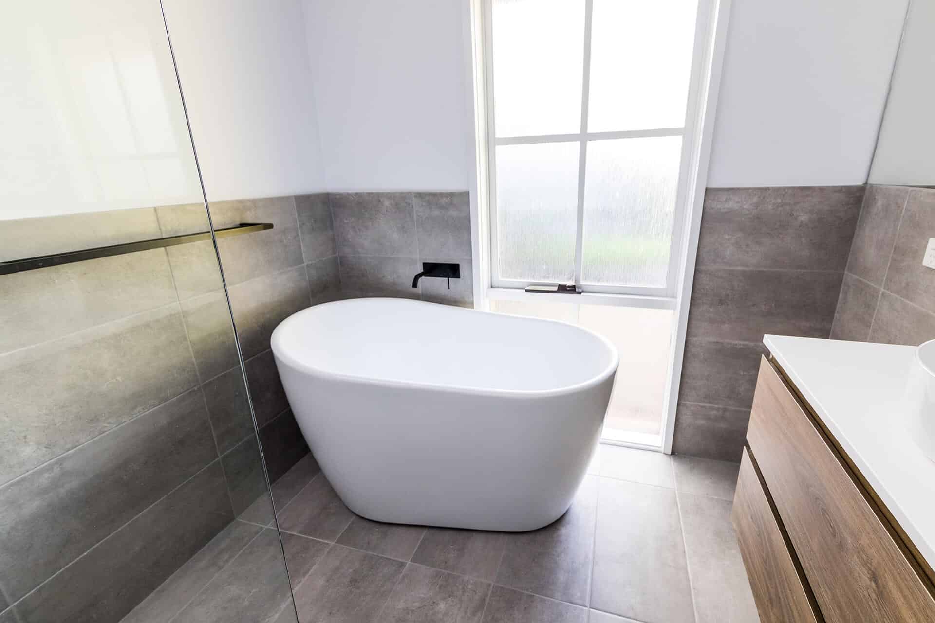 a white tub in a bathroom with a wooden vanity and a large window