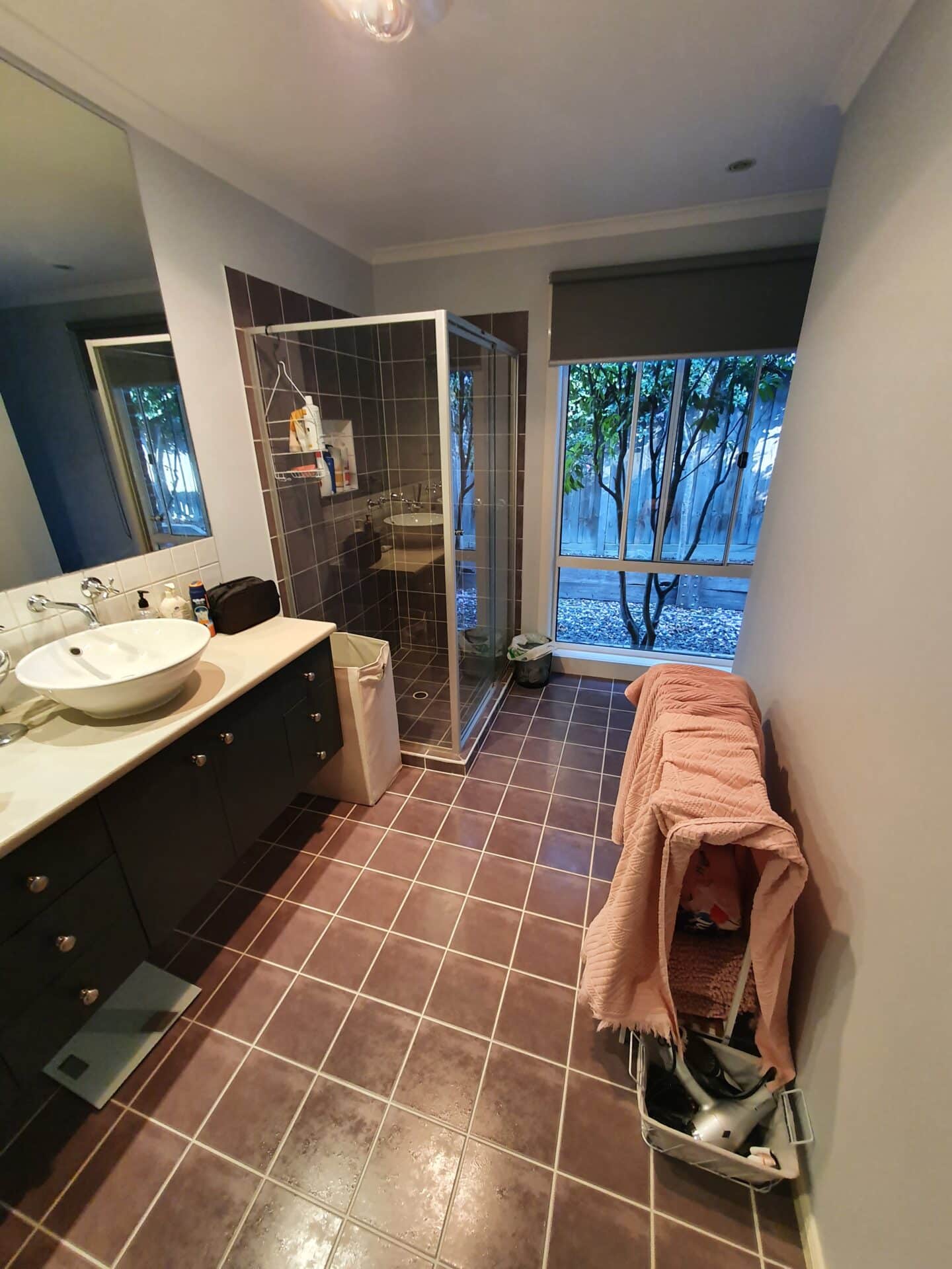 a bathroom with a shower, sink, large window and a dark red floor tiles
