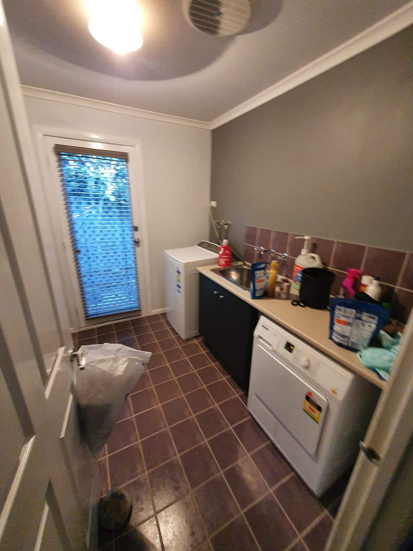 a laundry room with a sink, washing machine and maroon floor tiles