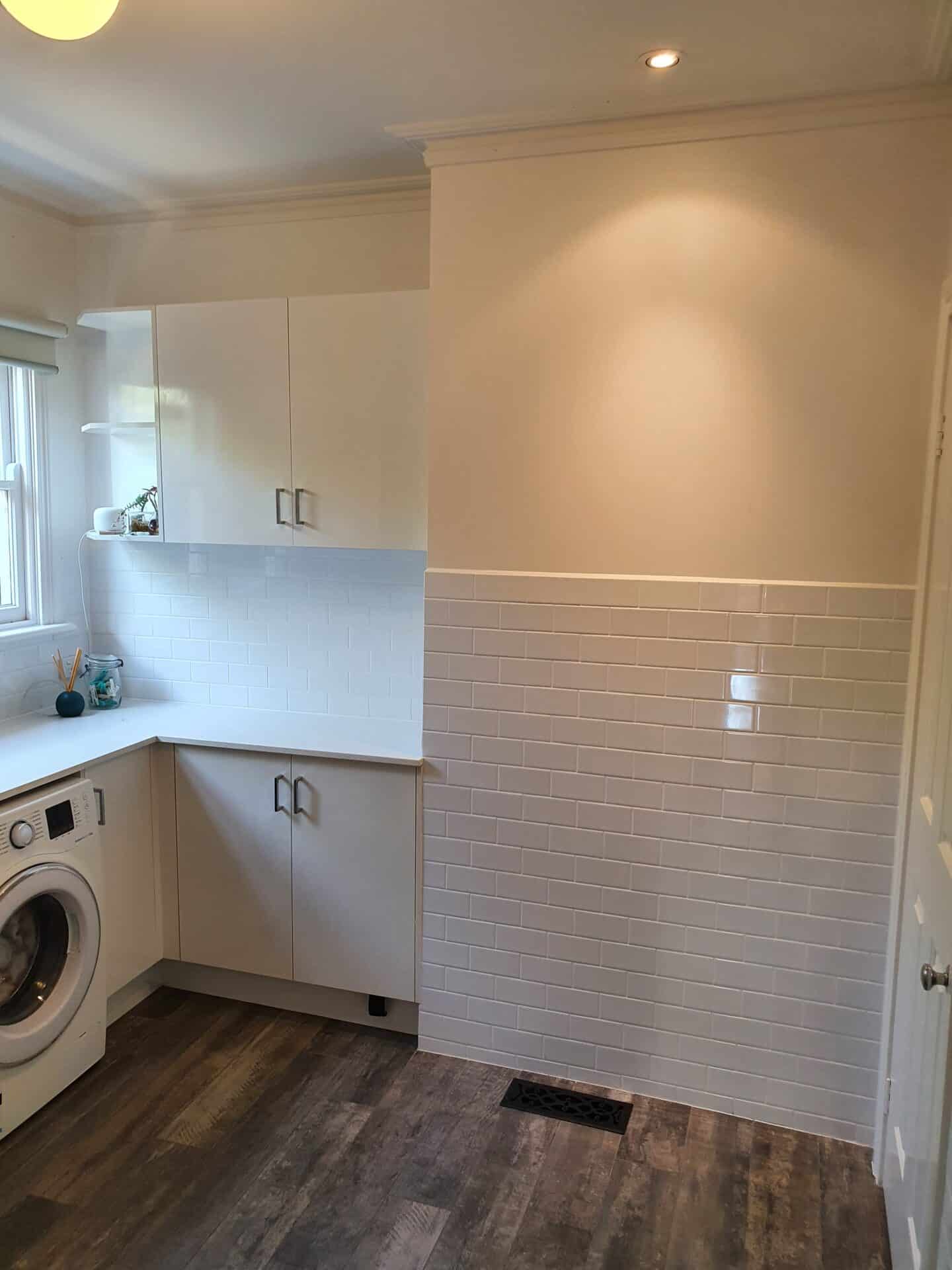 a white laundry room with white tile walls and a washing machine
