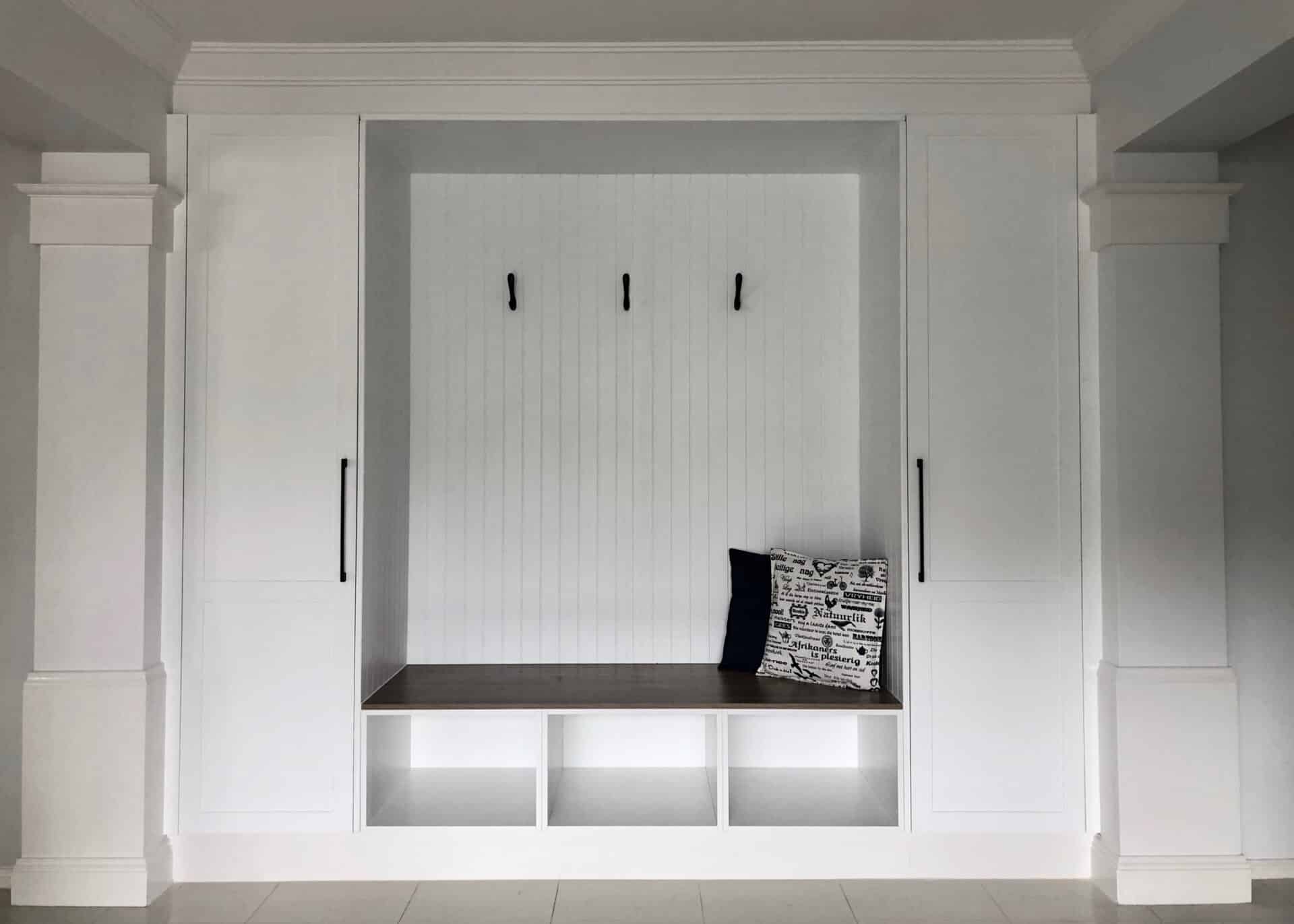 a white mudroom with pillows on a wooden bench