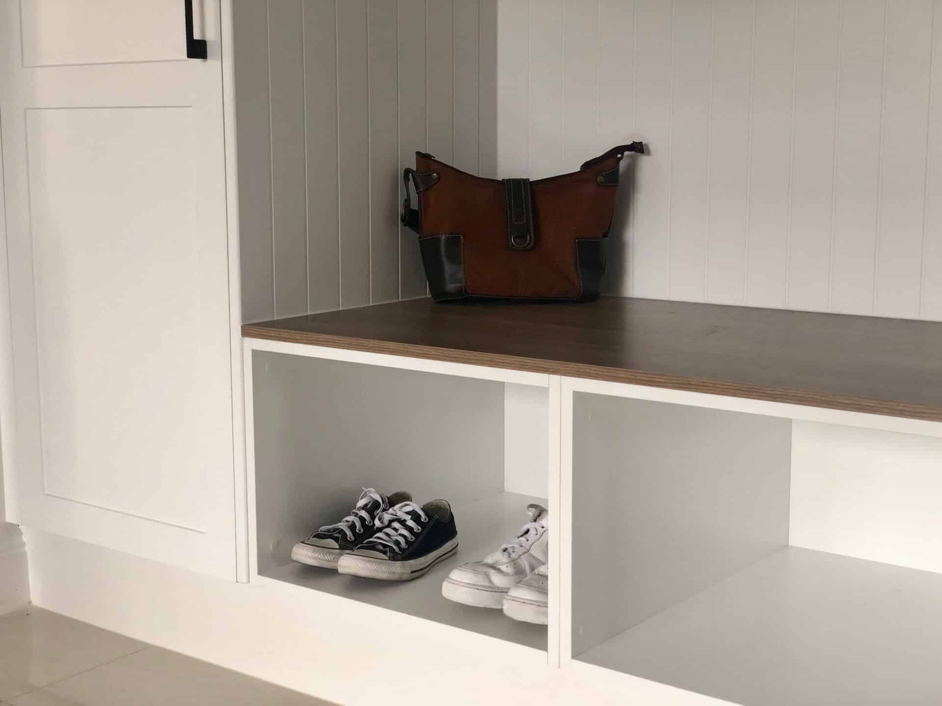 a pair of shoes on a white shelf and a bag above another wooden shelf