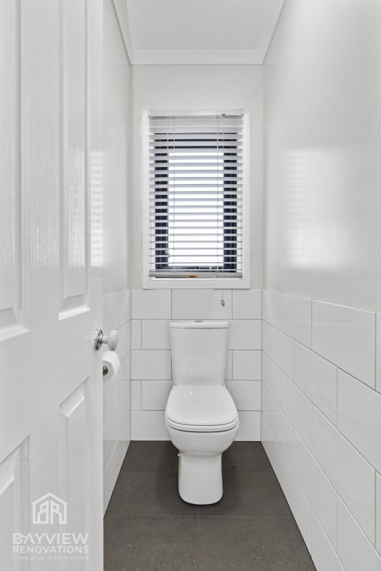 a white toilet in a bathroom with a small window above it