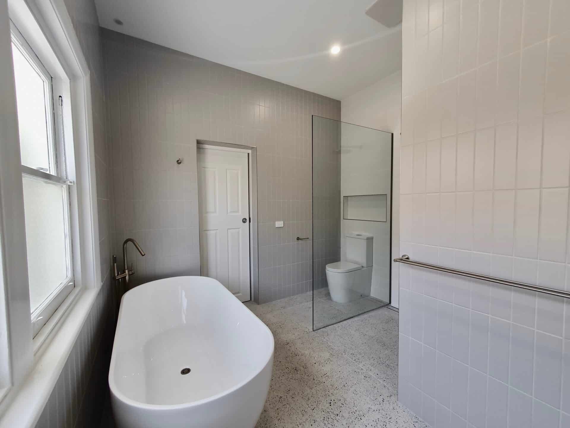 gray tiled bathroom with a bath tub, toilet and a shower glass