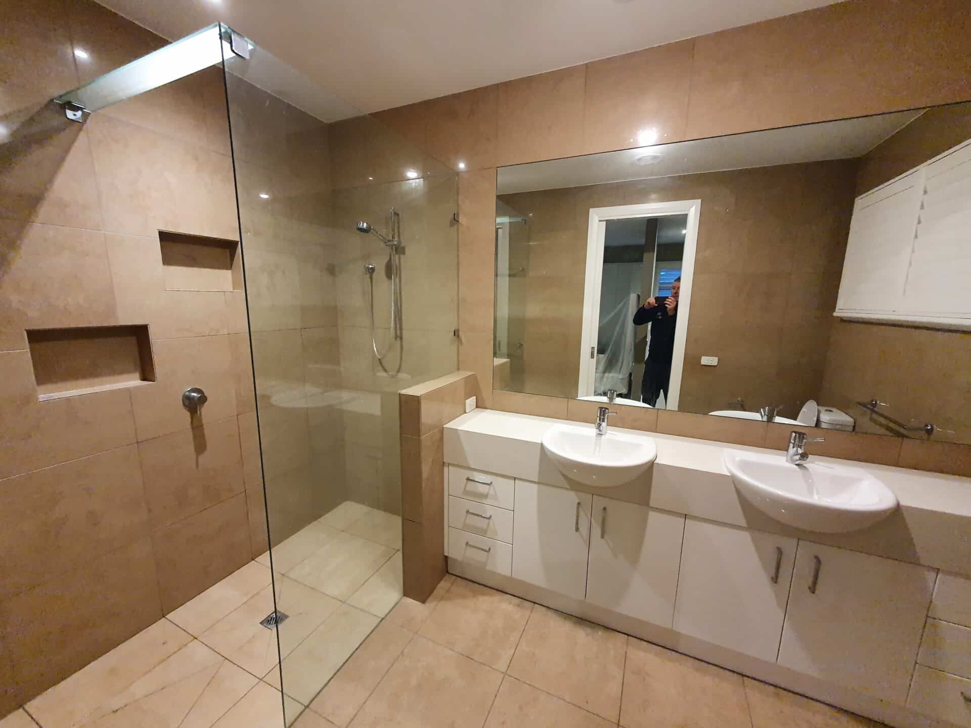 A modern renovated bathroom with double sinks, a glass shower and a large mirror.