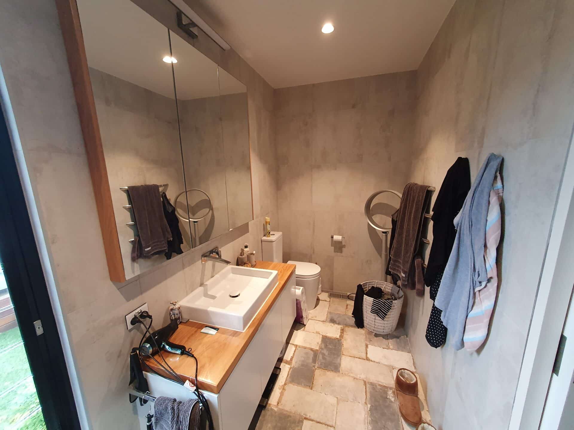 A bathroom with a sink and a mirror, and some clothes hanging.