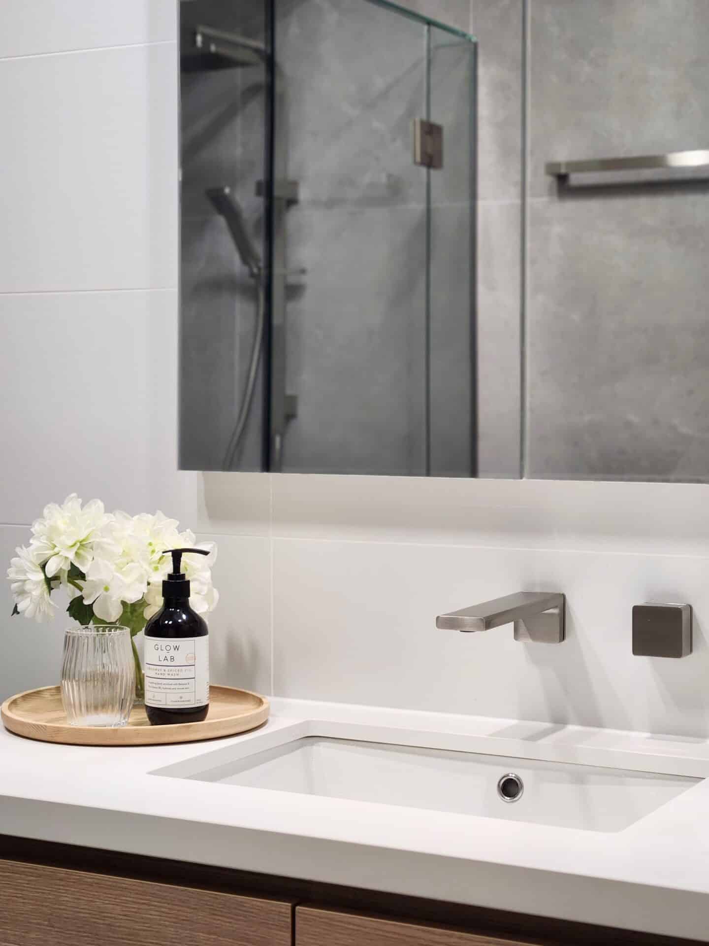 A bathroom sink with a mirror and a bottle of liquid on a tray.