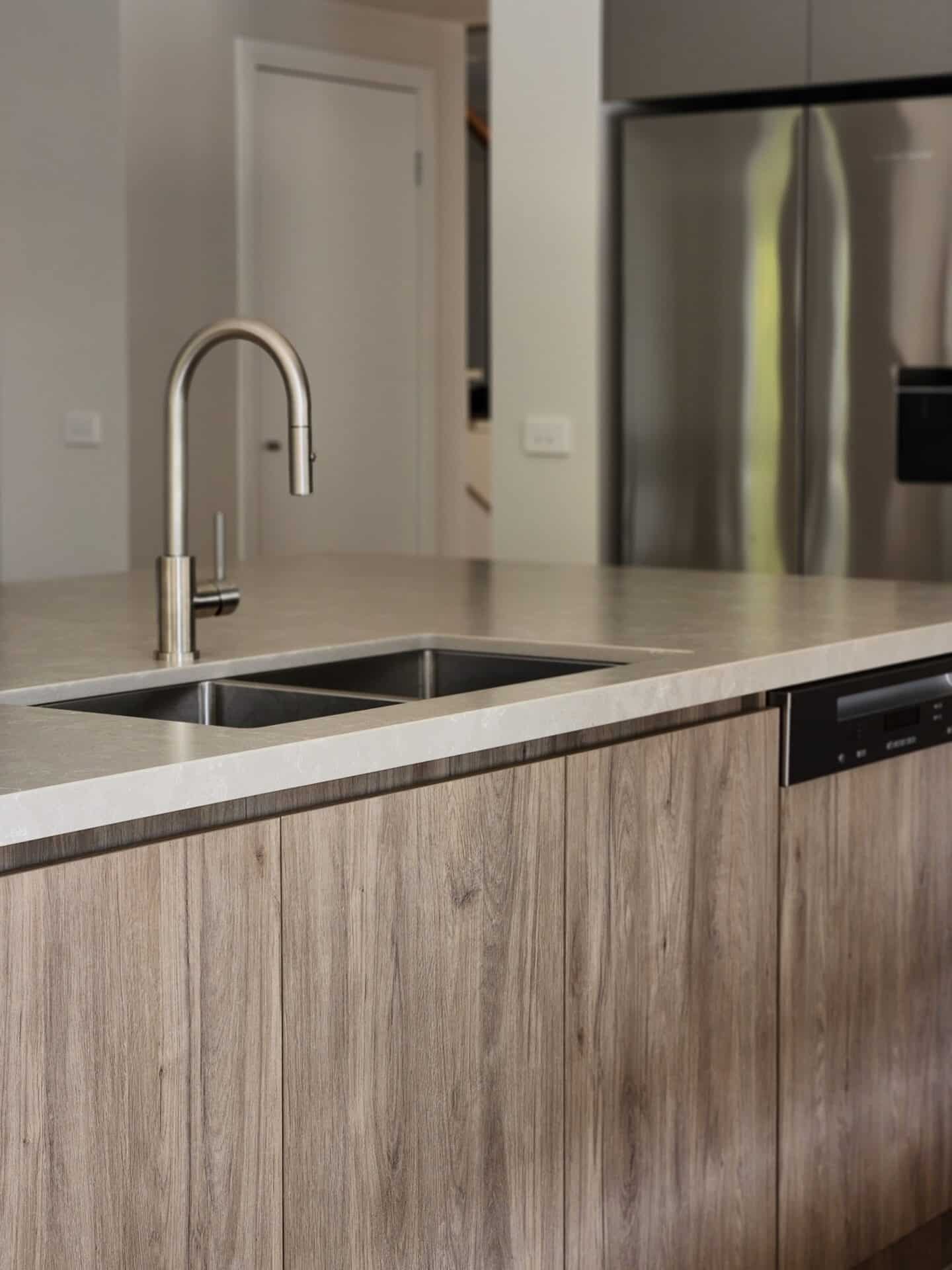 A kitchen sink with wooden cabinets and a large refrigerator behind.