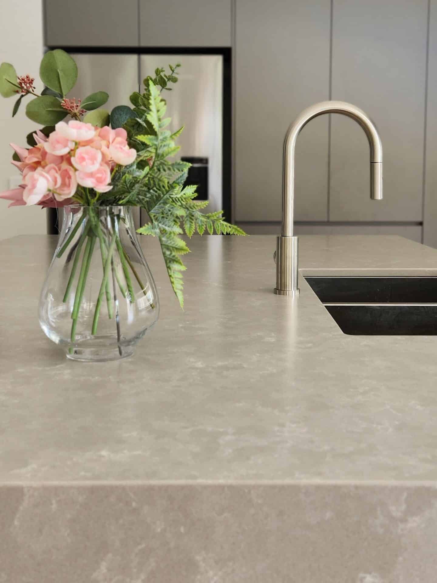 a marble kitchen sink with a flower vase and a refrigerator behind.