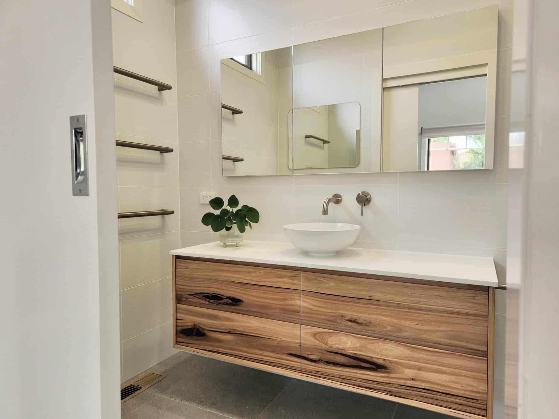 A white modern ensuite with wood cabinet and mirrors.