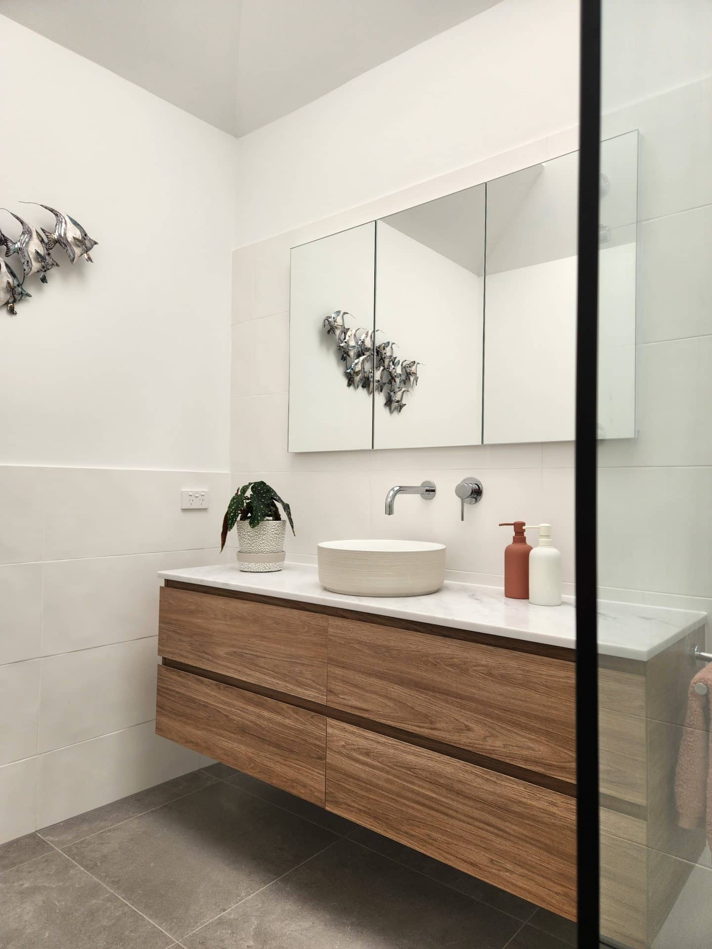 A modern bathroom with wooden cabinets and a glass shower undergoes renovations.