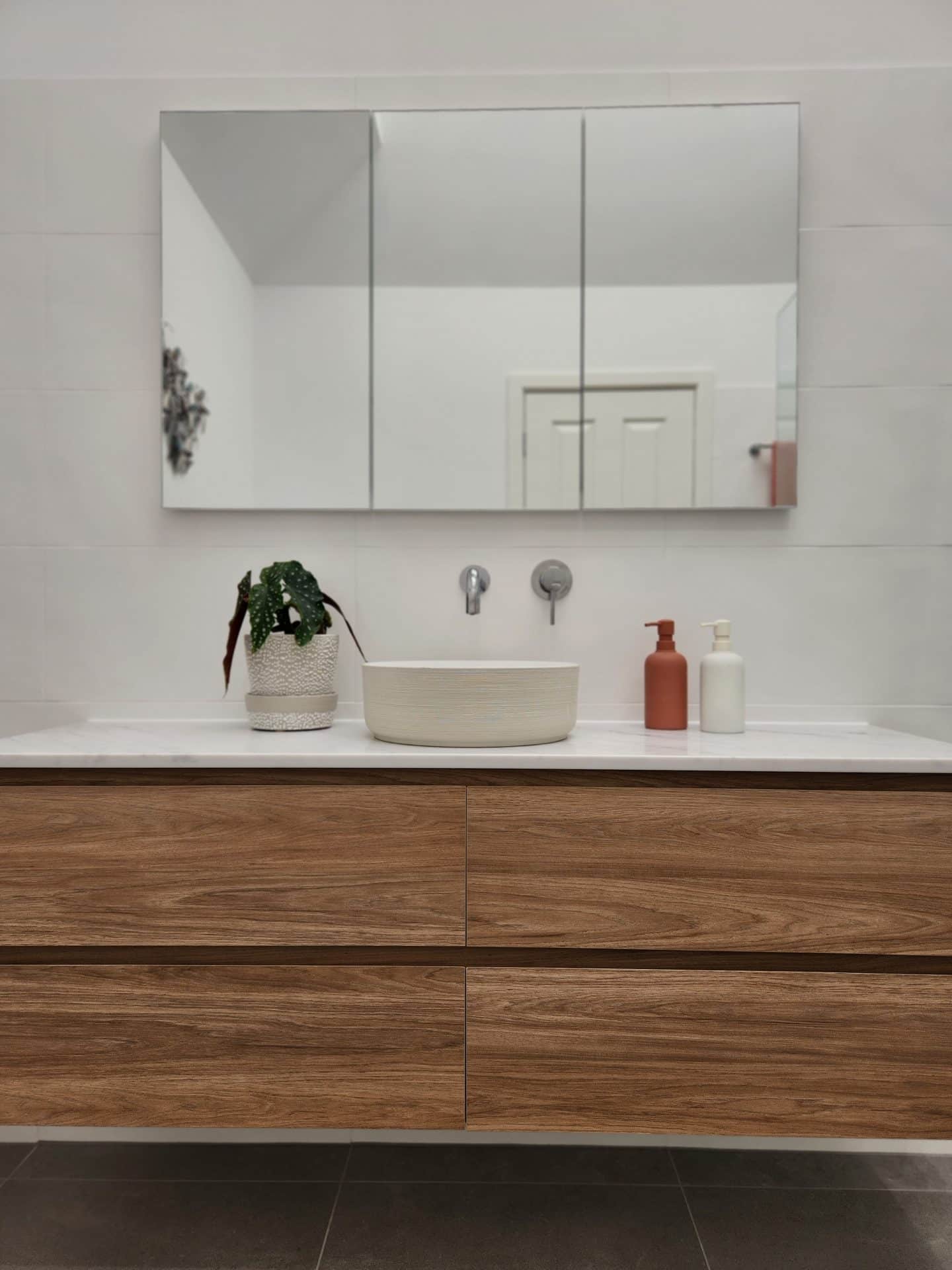 a renovated bathroom with a modern wooden vanity and mirror.
